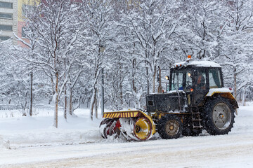 Snow plow tractor clears snow from the street during a snowfall. Snow-covered city street. Cold...