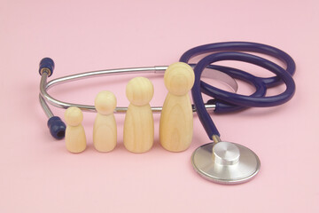 Family doctor concept. Big and small wooden people figures with stethoscope on pink background.