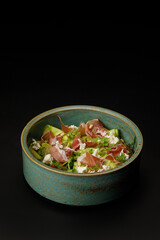 Pasta with prosciutto and fried zucchini over black background