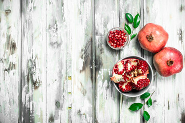 Grains and pieces of pomegranate in a bowl and whole pomegranates with leaves.