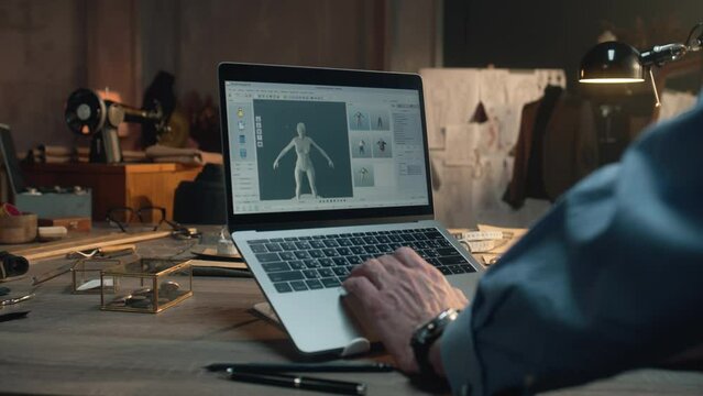 Male tailor or fashion designer creates clothes and develops future wear collection in 3D modeling program. He works in luxury designer workshop or tailoring studio on laptop. Fashion concept.