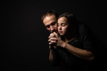 Young father and daughter praying with hands together with hope expression on face very emotional and worried.
