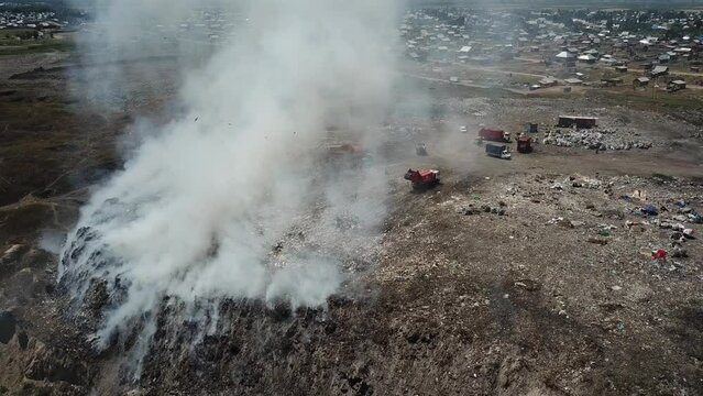 Drone flying over a smoking city dump. Landfill people.