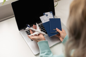 Positive happy woman going on summer holidays, sitting at office with toy plane and showing passport, having video call