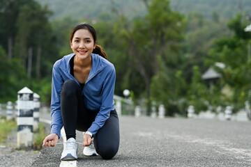 Smiling sportswoman tying shoelaces before running, getting ready for jogging outdoors. Healthy...