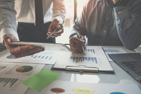 Two young Asian businessmen have a meeting on a real estate project. Planning and calculating, clarifying the information in the graph analyzing business finance charts, and accounting concepts.