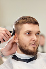 Barber trim hair with clipper on handsome bearded man