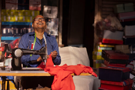 Portrait of a cheerful tailor swing clothes in his workshop