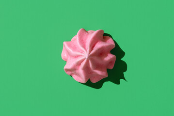 Pink meringue cookie minimalist on a green background, top view.