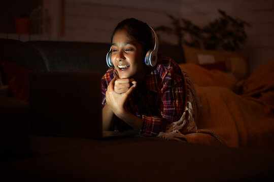 Girl watching video on laptop while lying down on sofa in living room