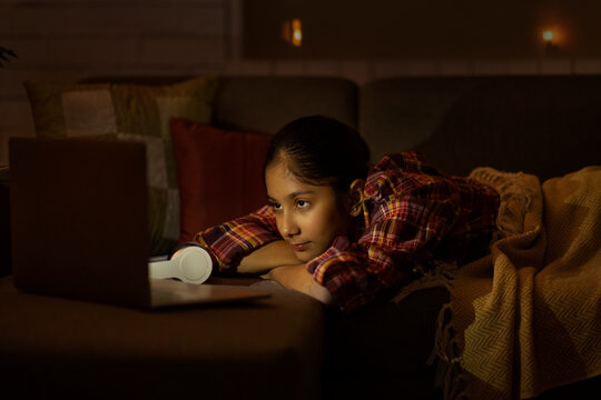 Girl watching video on laptop while lying down on sofa in living room