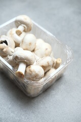 Champignon mushrooms in the plastic box at the grey background	