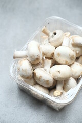 Champignon mushrooms in the plastic box at the grey background	