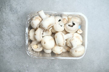 Champignon mushrooms in the plastic box at the grey background	