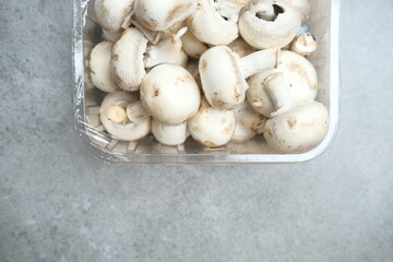 Champignon mushrooms in the plastic box at the grey background	