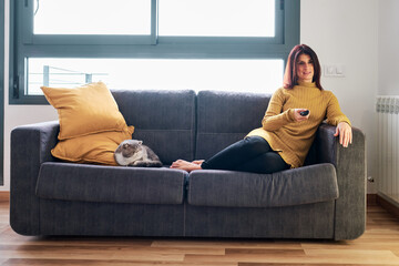 Woman watching television while relaxing sitting on the sofa with her cat.