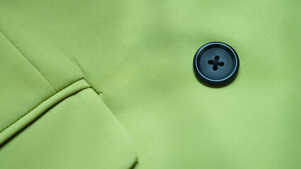 Black button is sewn on green cotton fabric closeup