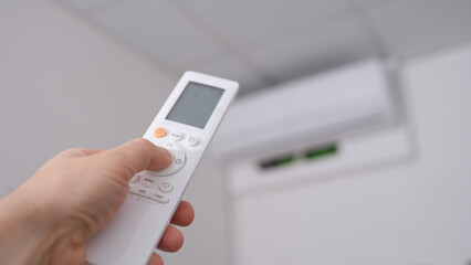 Woman hand holds remote control pointing at air conditioner in room