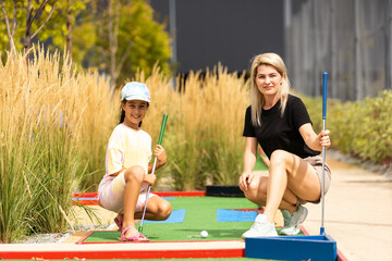 Detail of young woman and daughter playing mini adventure golf on a beautiful sunny summer day