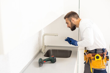 Young Repairman Installing Faucet Of Kitchen Sink In Kitchen Room