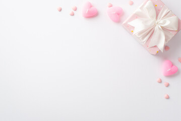 Obraz na płótnie Canvas Valentine's Day concept. Top view photo of pastel pink giftbox with silk ribbon bow sprinkles and heart shaped candles on isolated white background with empty space