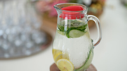Drink with lemon slices and cucumber in jug on table