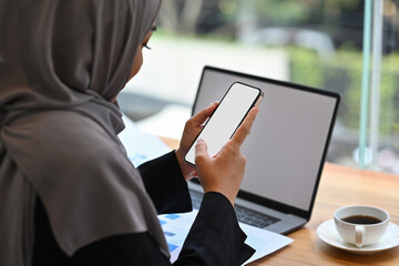 Behind shoulder view and cropped image of Arab businesswoman using smartphone and laptop, Empty screen of devices, Business and financial concept.