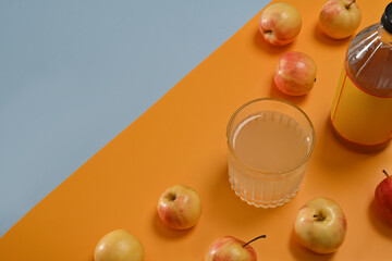 Top view with Apple cider vinegar in the bottle and glass and small apples decorated on the yellow and plain blue background.