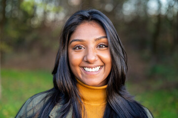 Portrait of a yong Indian woman in the nature, head shot of a teenager looking at the camera in a public park