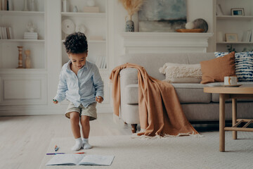 Happy mixed race little boy enjoying playing alone at home, having fun in living room