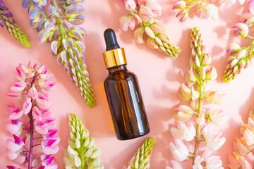Cosmetology product for facial care. Serum in glass bottle with pipette and pink lupine flowers on pink background. Essential oil for care of skin. Skin care, mockup