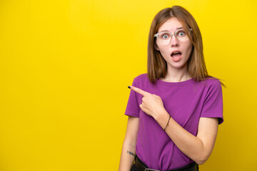 Young English woman isolated on yellow background surprised and pointing side