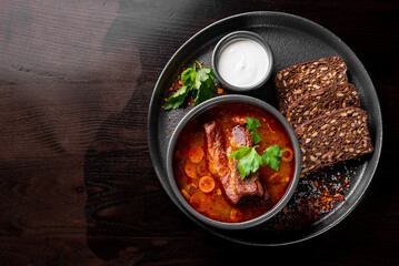 Solyanka soup with meat, sausage, vegetables, olives and lemon in bowl on wooden table background
