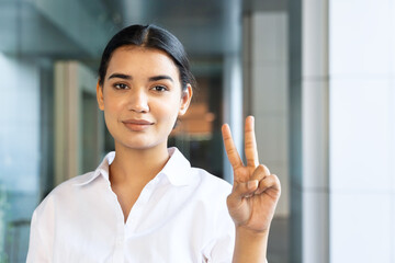 Happy smiling young south asian Indian woman pointing up 2 fingers, showing V for victory, number...