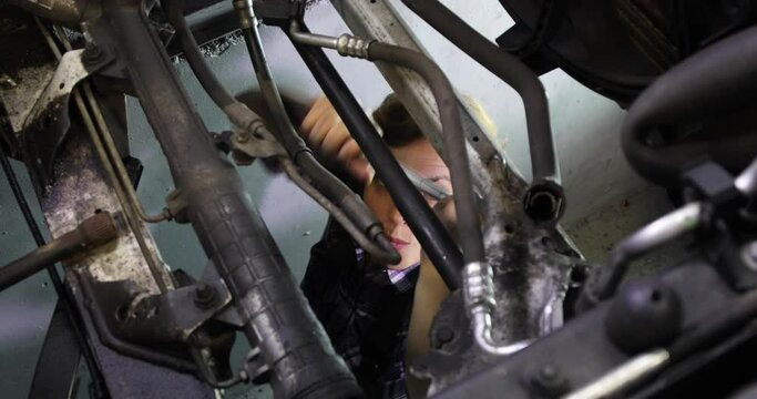Woman mechanic working under a car with her wrench. Working day and night in her customs shop