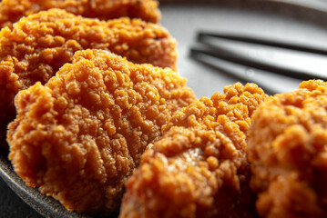 Close up, Spicy pieces of chicken fillet in crispy breading, on a black plate on a dark background,...