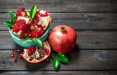 Pieces of ripe pomegranate in bowl and one ripe pomegranate with leaves.