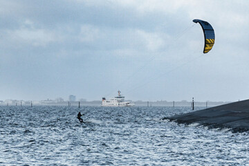 Ein Kitesufer an der Küste der rauen Nordsee mit einer Fähre im Hintergrund