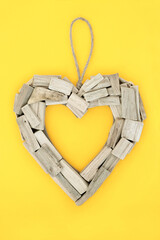 Driftwood heart shaped rustic wreath symbol of love and romance. Natural  weathered romantic frame for Valentines Day, Mothers Day, anniversary and birthday. On yellow background,