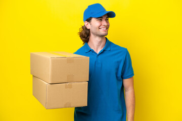 Fototapeta na wymiar Delivery handsome man isolated on yellow background looking to the side and smiling