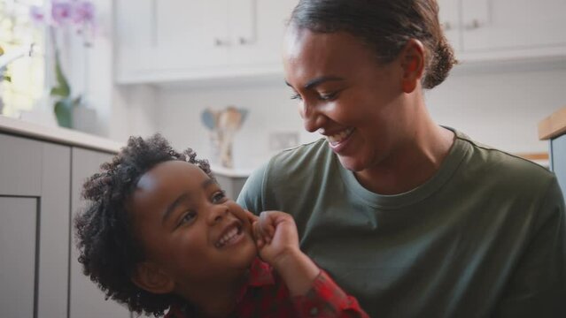 Army Mother In Uniform Home On Leave Playing With Son In Family Kitchen