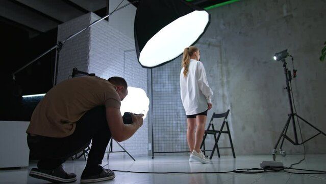 Camera man taking picture of a model in studio. Photographer squatted to take a picture of a female standing her back to him.
