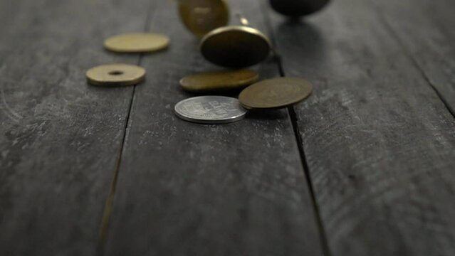 Antique and modern coins fall on a black wooden board, slow motion