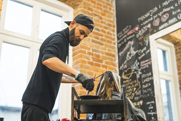 bearded hairdresser in black clothes dying client's hair, salon medium shot. High quality photo