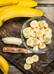 Bananas and banana slices in a plate on a black chopping Board with a knife.