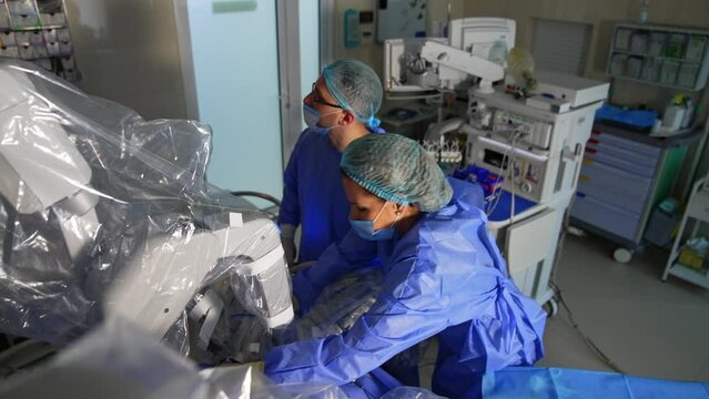 Male surgeon and assisting nurse working in cooperation with robotic equipment. Modern surgery room with Da Vinci machine performing operation. Top view.