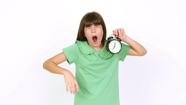 Little girl holding vintage alarm clock and yawning over isolated background