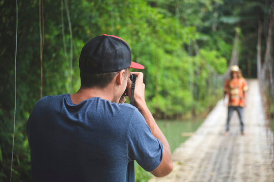 Rear view of man photographing friend while standing on rope bridge