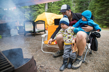 Father roasting marshmallows at campsite with his two kids