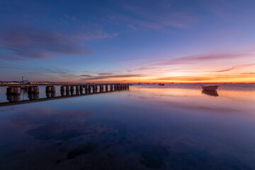 Beautiful seascape at sunrise in the Mar Menor, Los Alcazares, Spain. With a spectacular sky, very colorful and reflected in the calm waters of the sea. We also see a wooden jetty and boats on the wat